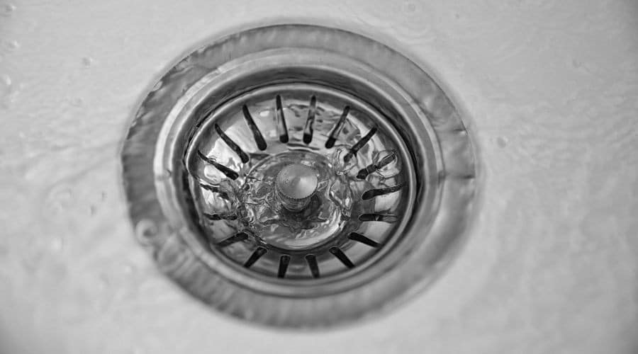 Close-up of a sink drain with water flowing, illustrating common plumbing issues related to blocked drains.