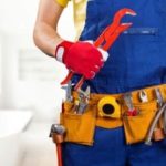 Worker in yellow shirt and blue overalls holds adjustable wrench, ready for plumbing service and leak detection.
