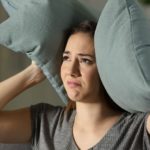 Woman looking distressed indoors with two soft blue-gray pillows, emphasizing plumbing service's leak repair focus.