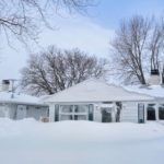 Snow-covered house with visible roof and trees, illustrating winter conditions relevant to plumbing maintenance and pipe protection advice.