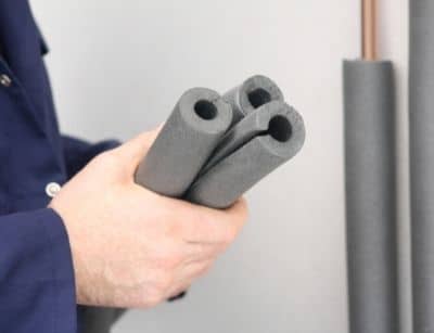 Person holding three pieces of foam pipe insulation, highlighting preventive measures for protecting plumbing from freezing temperatures.