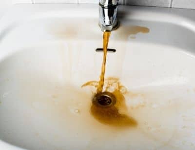 Rust-colored water flowing from a faucet into a sink, indicating potential corrosion in a water heater, relevant to plumbing maintenance and replacement.