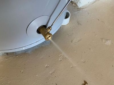 Brass valve on a water heater releasing water during flushing process to remove mineral buildup for efficient operation.