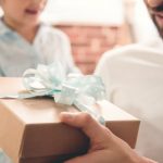 Father receiving a gift box with a blue ribbon from a child, symbolizing thoughtful Father's Day plumbing upgrades.