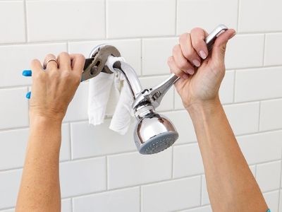 Hands using pliers to remove an old showerhead in a bathroom setting, illustrating a simple plumbing upgrade for Father's Day.