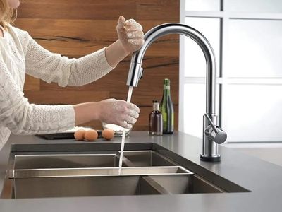Woman using a modern kitchen faucet to wash dishes in a sleek, contemporary kitchen, highlighting the benefits of upgraded fixtures for comfort and functionality.