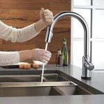 Person using a modern kitchen faucet with a pull-down sprayer, demonstrating functionality in a stylish kitchen setting, relevant to plumbing upgrades for guest comfort.
