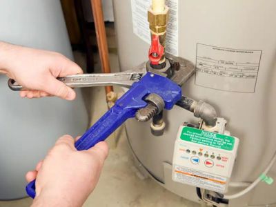 Hands using a wrench to adjust a water heater valve, emphasizing essential water heater maintenance tasks for homeowners.
