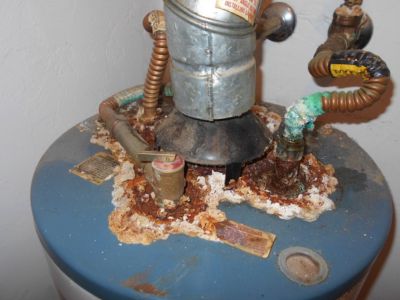 Corroded water heater tank showing rust, sediment buildup, and deteriorating pipes, indicating signs of corrosion and potential need for replacement.