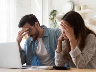 Frustrated couple reviewing high utility costs on a laptop, highlighting concerns about water heater efficiency and potential repairs.